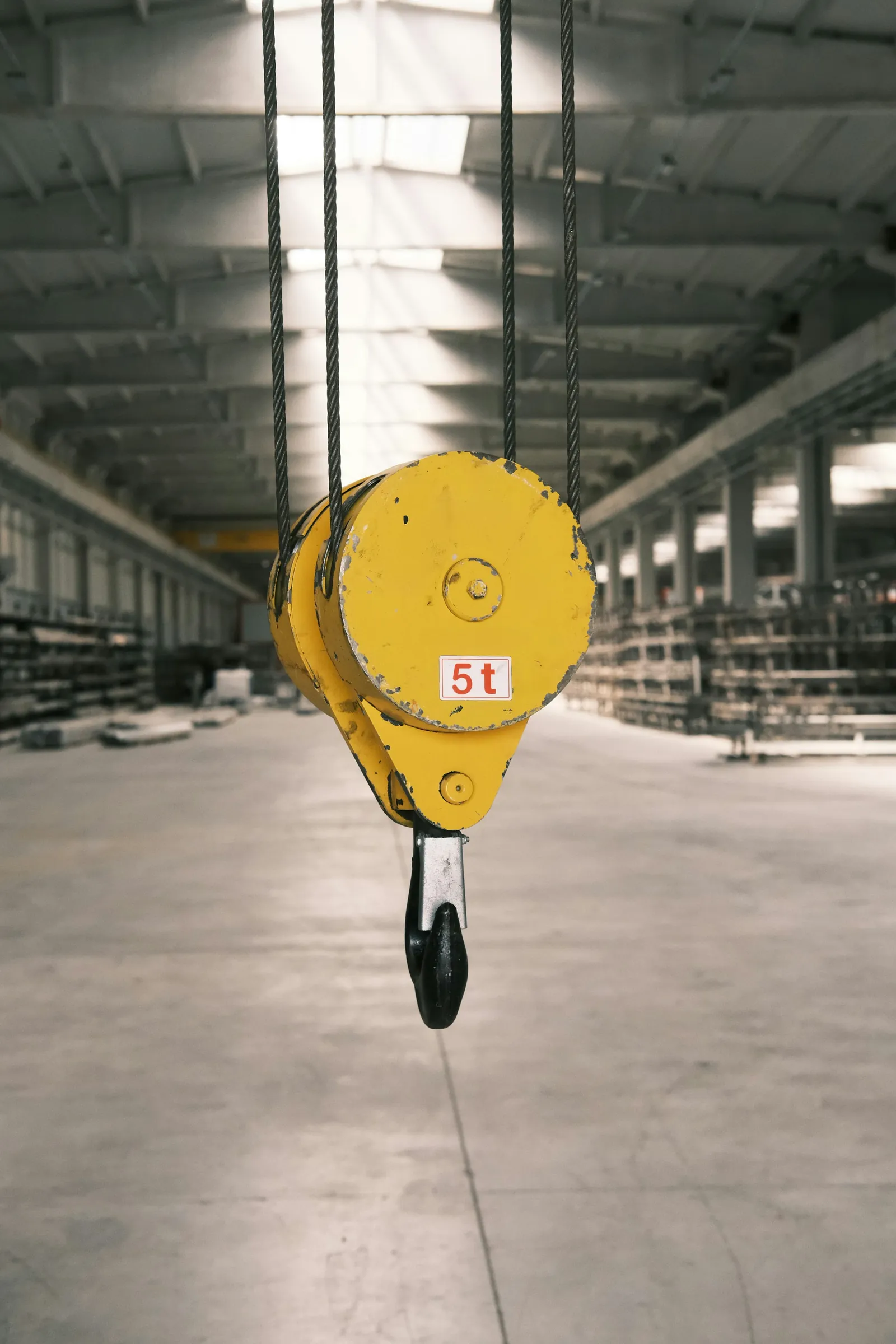 Yellow overhead crane hook in a bright steel warehouse