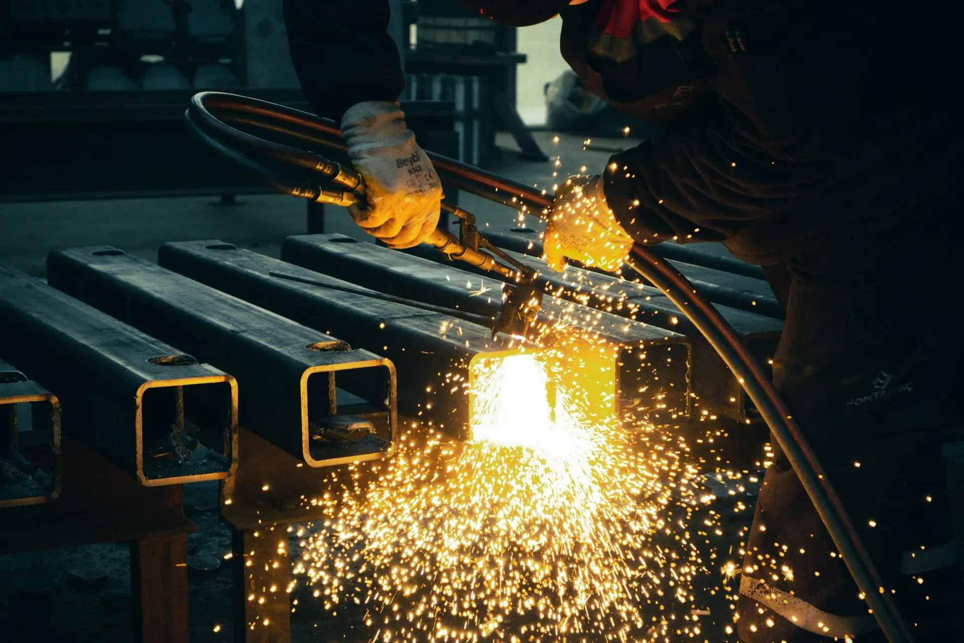 Fabricator cutting square steel tubes with sparks
